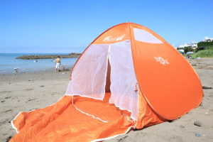 オレンジのポップアップテントを海で広げている写真
